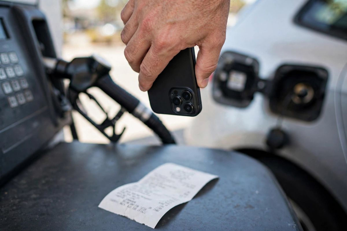 Hand photographing a gas station receipt with a phone at the fuel pump